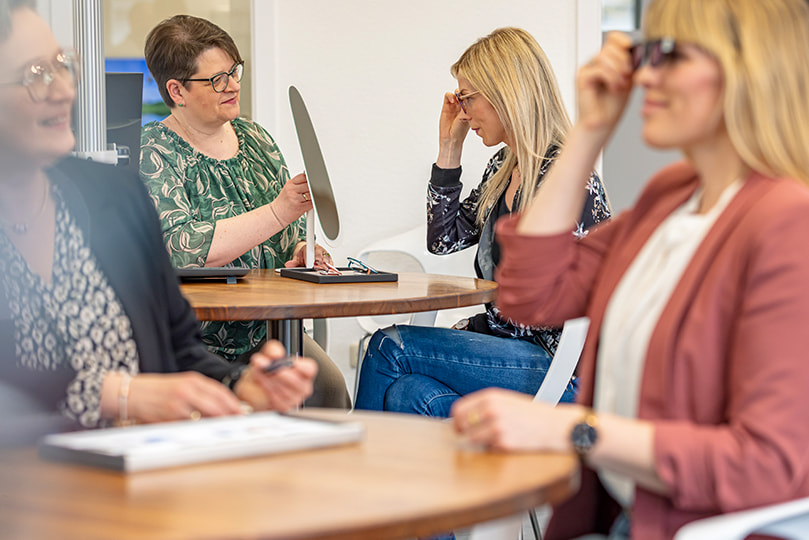 Augenoptikerinnen im Beratungsgespräch mit ihren Kundinnen zur Auswahl von Brillengläsern mit UV-Schutz und individuellen Tönungen.
