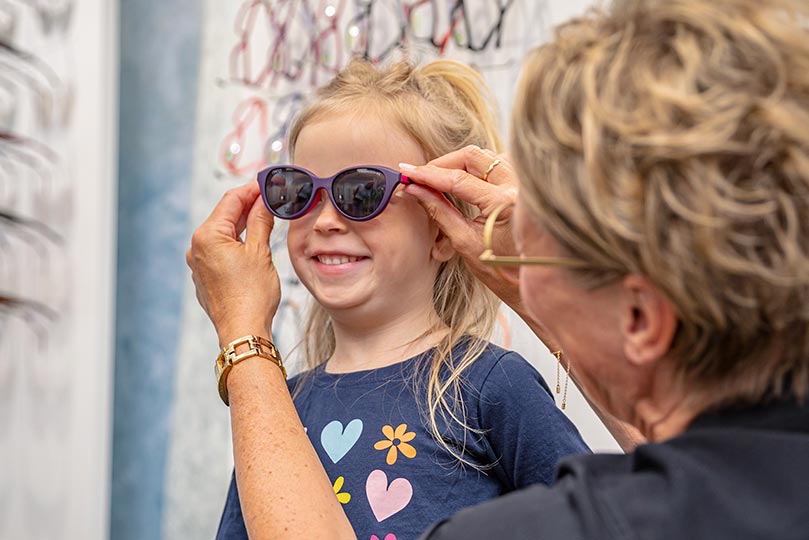 Ein Kind beim Test einer Brille mit integriertem Sonnenbrillenclip, der effektiven UV-Schutz bietet.