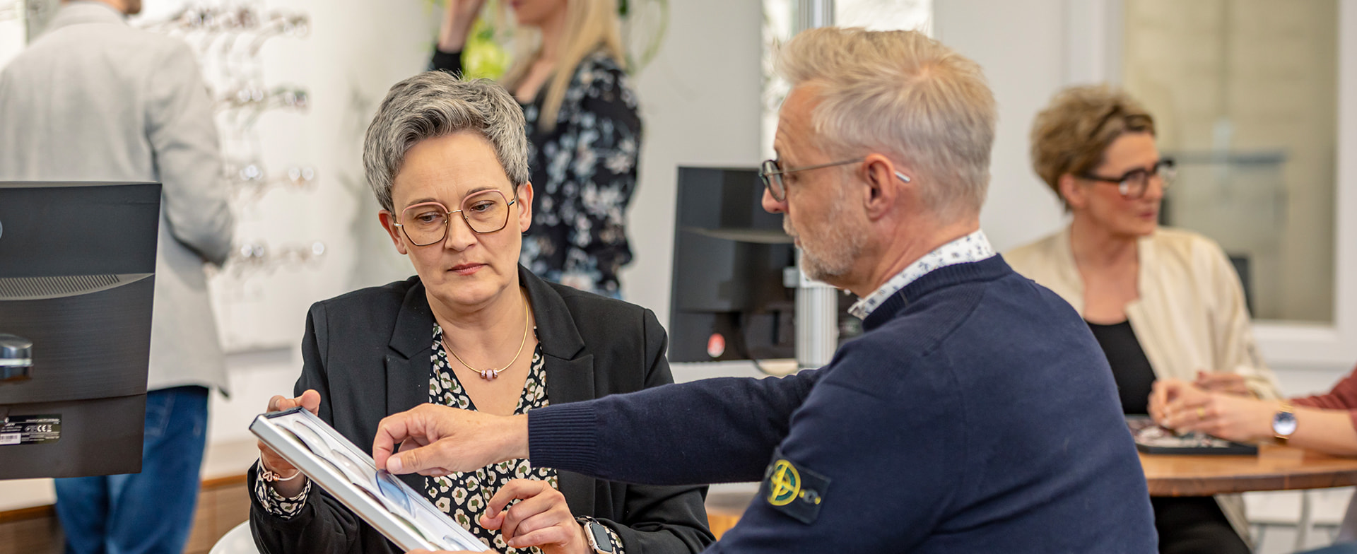 Augenoptikerin im persönlichen Beratungsgespräch mit einem Kunden zur Auswahl der optimalen Brille für individuelle Sehbedürfnisse.