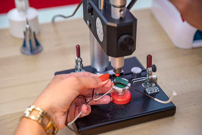 Augenoptikerin nutzt einen speziellen Bohrer in der Werkstatt, um die Schließblock-Schraube einer Metallbrille sorgfältig auszubohren.