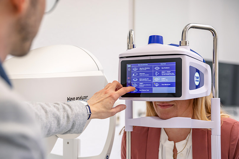 Augenoptiker analysiert mit Kundin den Tränenfilmaufbau und die Tränenfilmqualität am Tearcheck-Messgerät.